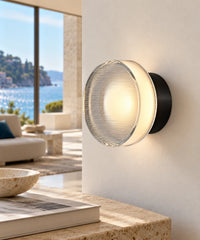 Applique ronde à fines stries horizontales, monture noire, près d’une console dans un séjour lumineux.