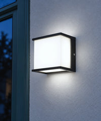Applique noire allumée d’une lumière blanche sur une façade bleue