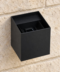 Vue rapprochée par le dessus du boîtier noir d’une applique cube fixée sur un mur en pierre