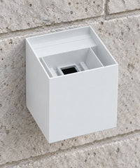 Vue rapprochée par le dessus du boîtier blanc d’une applique cube sur un mur en pierre