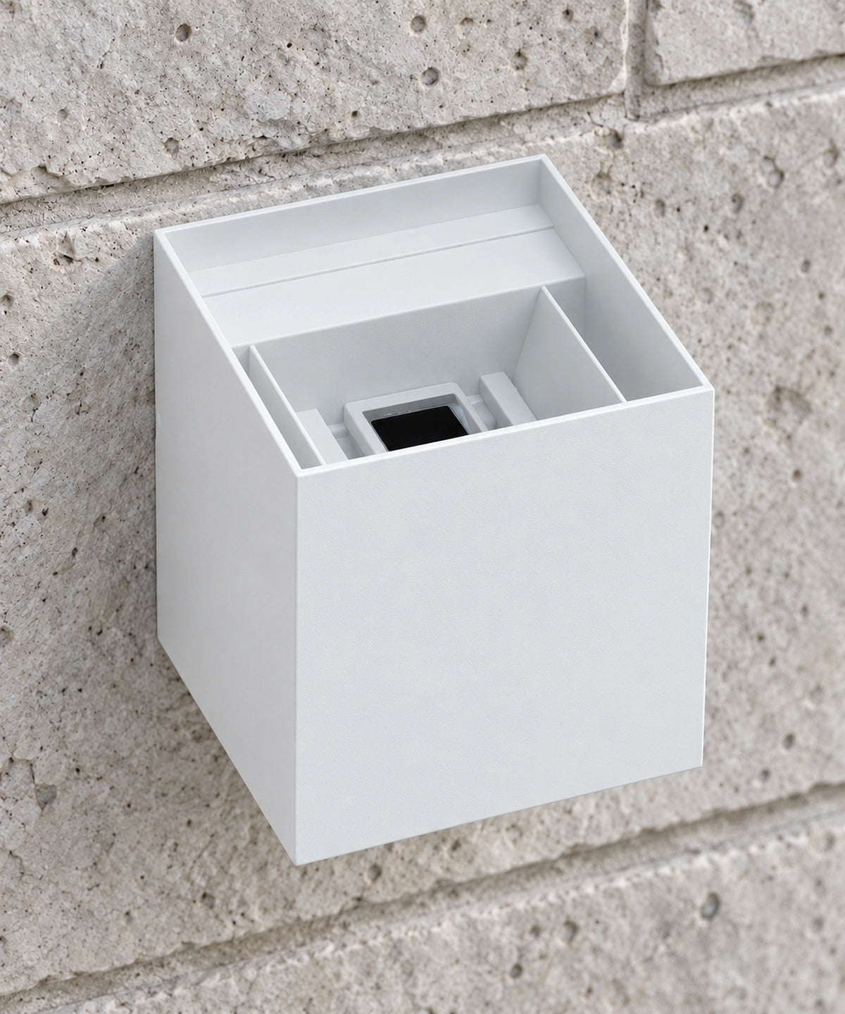 Vue rapprochée par le dessus du boîtier blanc d’une applique cube sur un mur en pierre