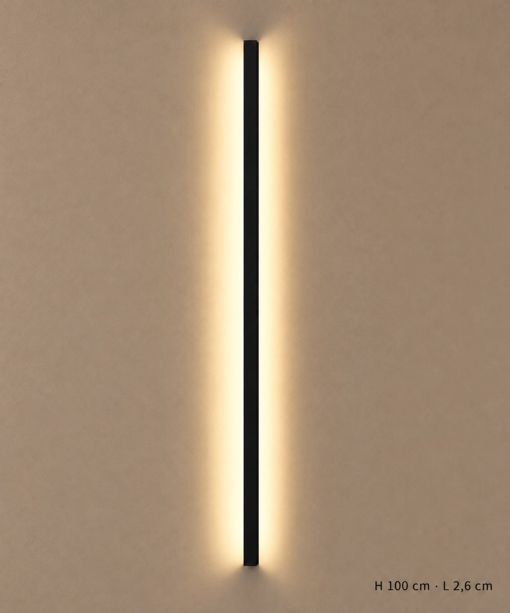 Applique longue noire de 100 cm allumée sur un mur clair, avec dimensions indiquées