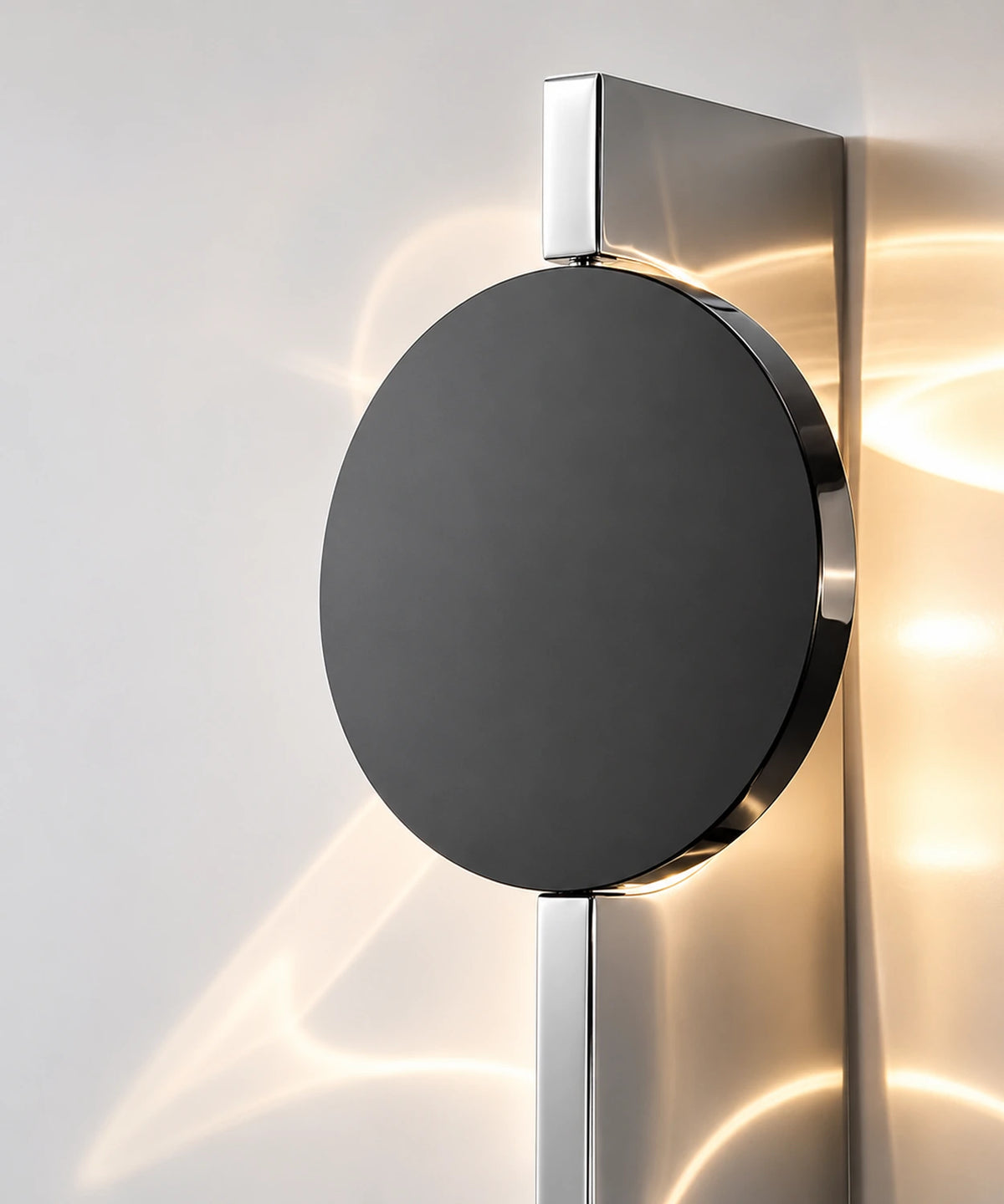 Gros plan sur le disque noir et la plaque d’inox poli miroir de l’applique