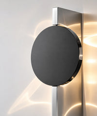 Gros plan sur le disque noir et la plaque d’inox poli miroir de l’applique