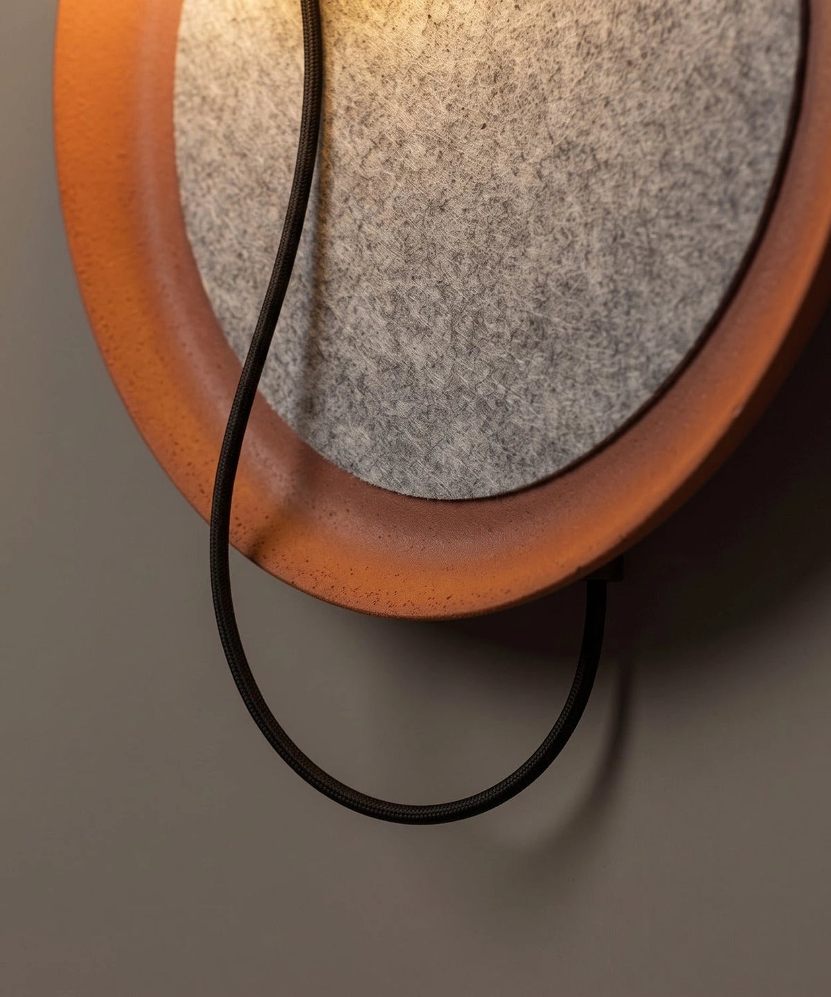 Détail du câble noir en boucle sous le disque de feutre cerclé de terracotta