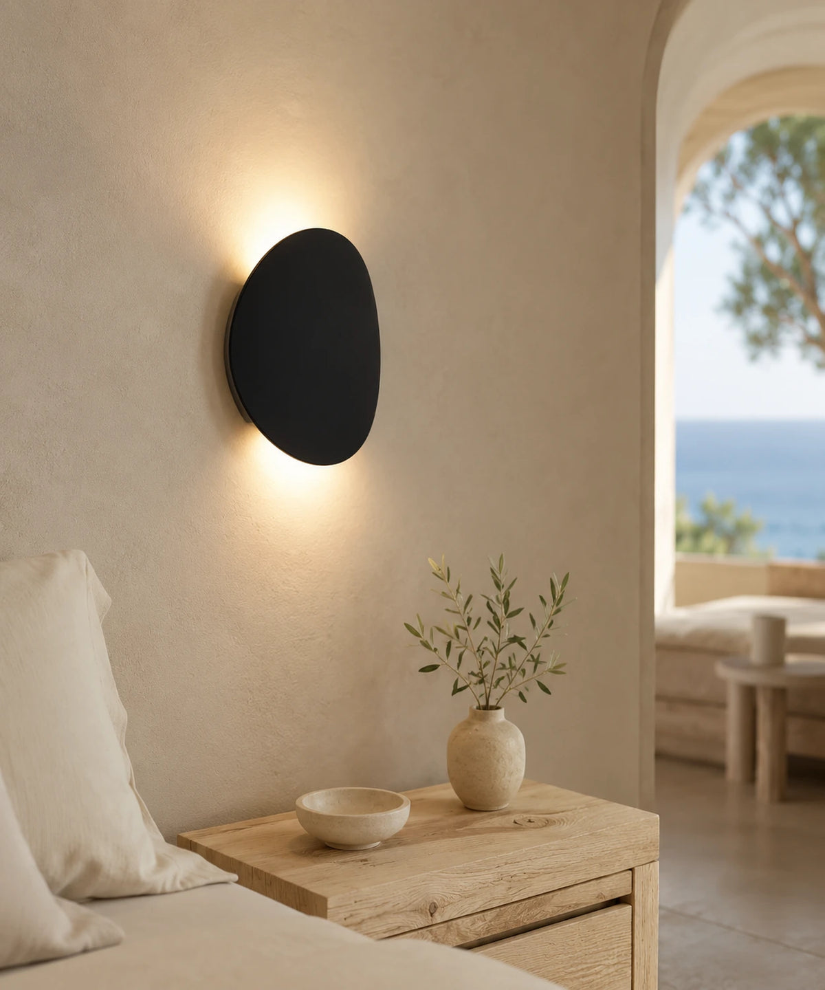 Applique murale forme galet noir sable en tête de lit, halo de lumière sur le mur