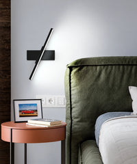 Applique murale LED orientable noire près d’un lit vert, barre inclinée et diffuseur linéaire allumé