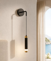 Applique murale tube suspendu noir et or allumée sur un mur enduit, fenêtre sur la mer