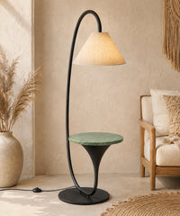 Lampadaire arc avec tablette en marbre vert allumé près d’un fauteuil en bois