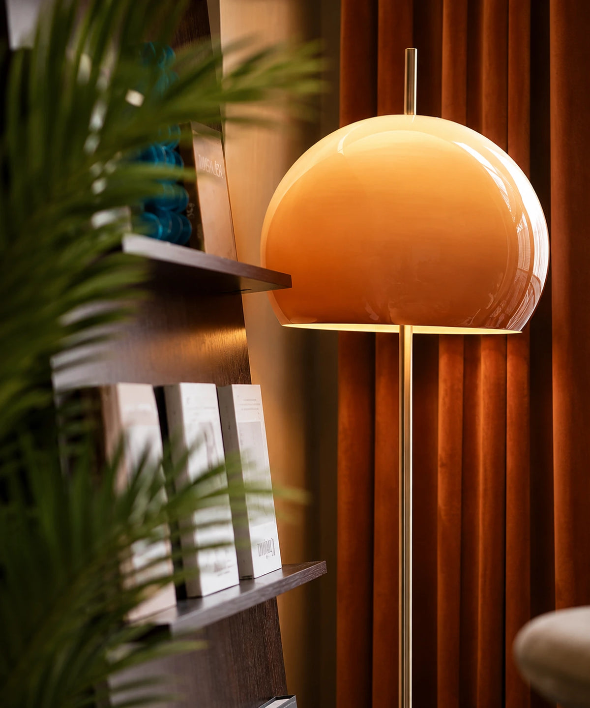 Lampadaire champignon chromé au dôme dégradé orange devant une bibliothèque et des rideaux