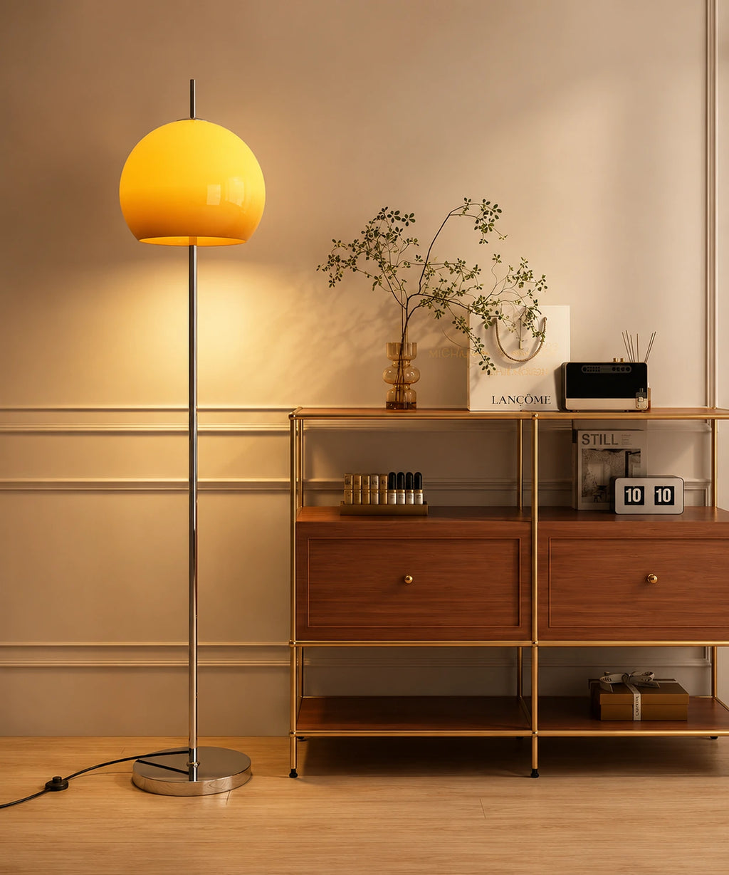 Lampadaire champignon chrome allumé à côté d’une étagère en bois et laiton