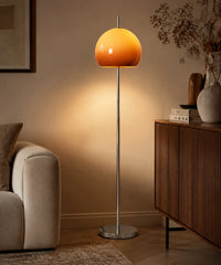 Lampadaire champignon chrome à dôme de verre orange allumé dans un salon, à côté d’un canapé