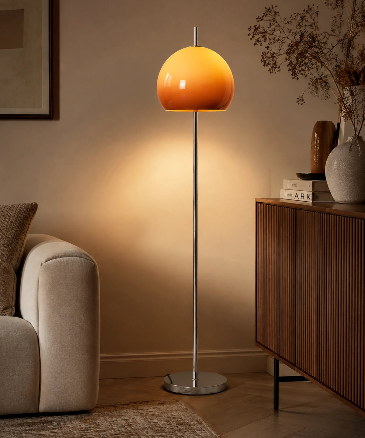 Lampadaire champignon chrome à dôme de verre orange allumé dans un salon, à côté d’un canapé