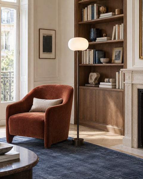Lampadaire en bronze et verre opalin près d’un fauteuil terracotta, dans une bibliothèque lumineuse