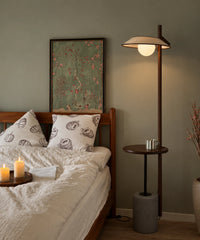Lampadaire liseuse avec tablette au chevet d’un lit en bois, globe opalin allumé