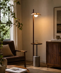 Lampadaire liseuse en bois et ciment allumé près d’un fauteuil de lecture et d’une fenêtre