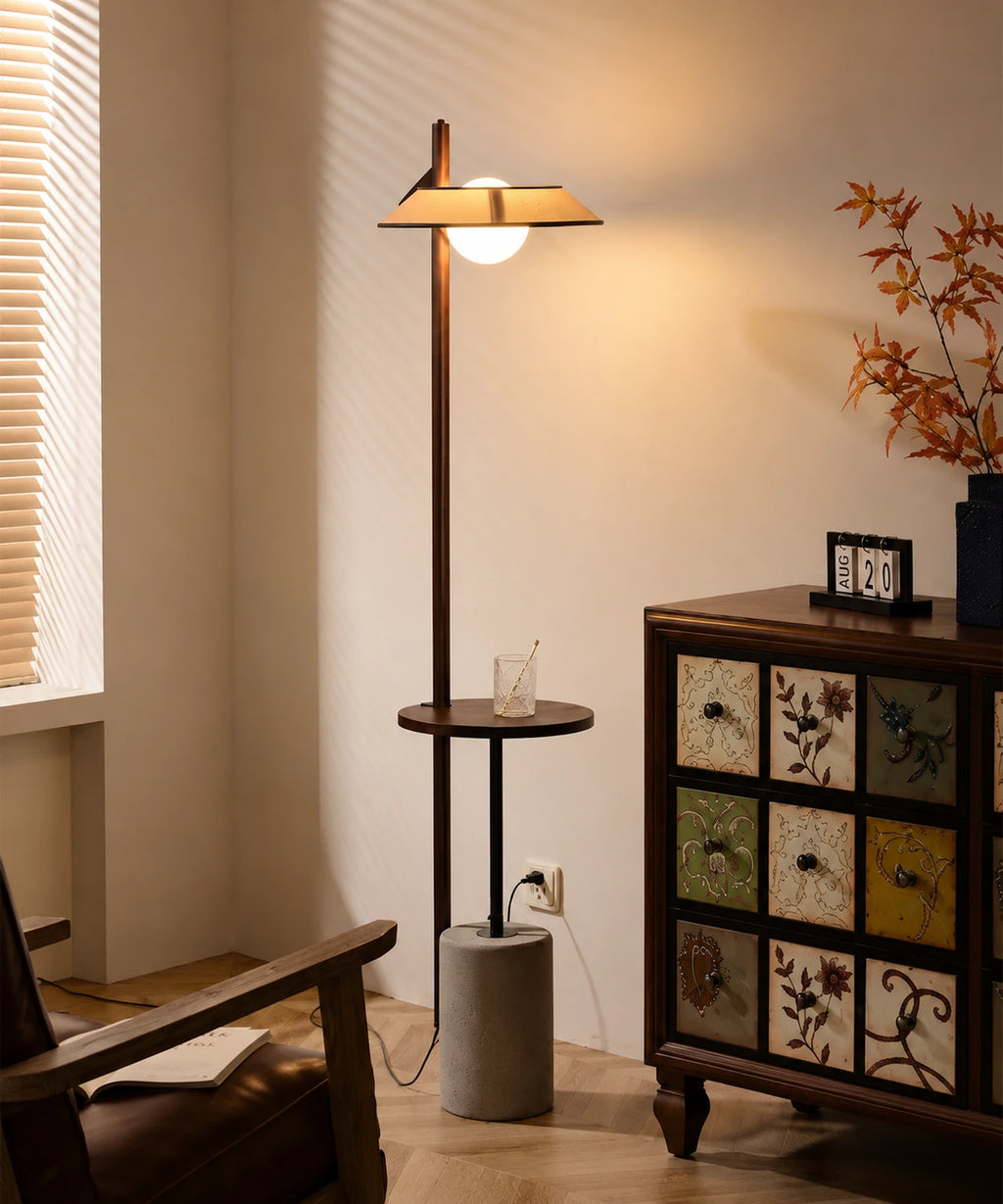 Lampadaire liseuse avec tablette allumé dans un salon, à côté d’un fauteuil en cuir et d’une commode