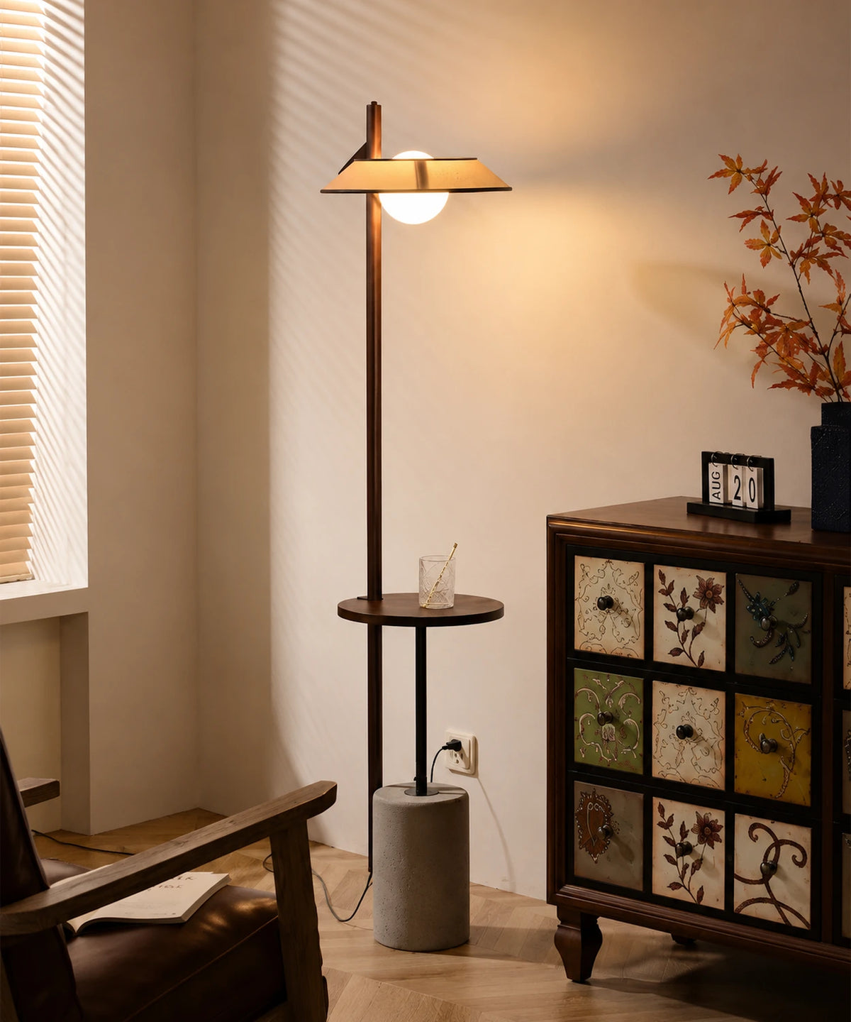 Lampadaire liseuse avec tablette allumé dans un salon, à côté d’un fauteuil en cuir et d’une commode