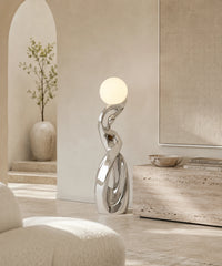 Lampadaire sculpture chrome argent allumé sous une arche, banc en travertin