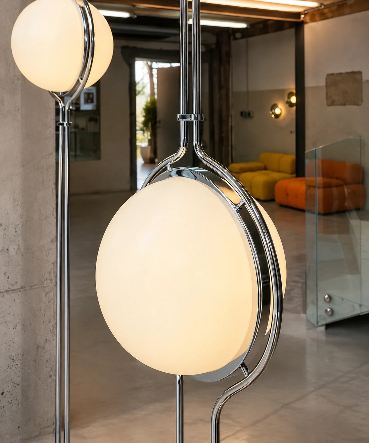 Gros plan sur l’anneau chromé et la boule opaline allumée du lampadaire sol-plafond