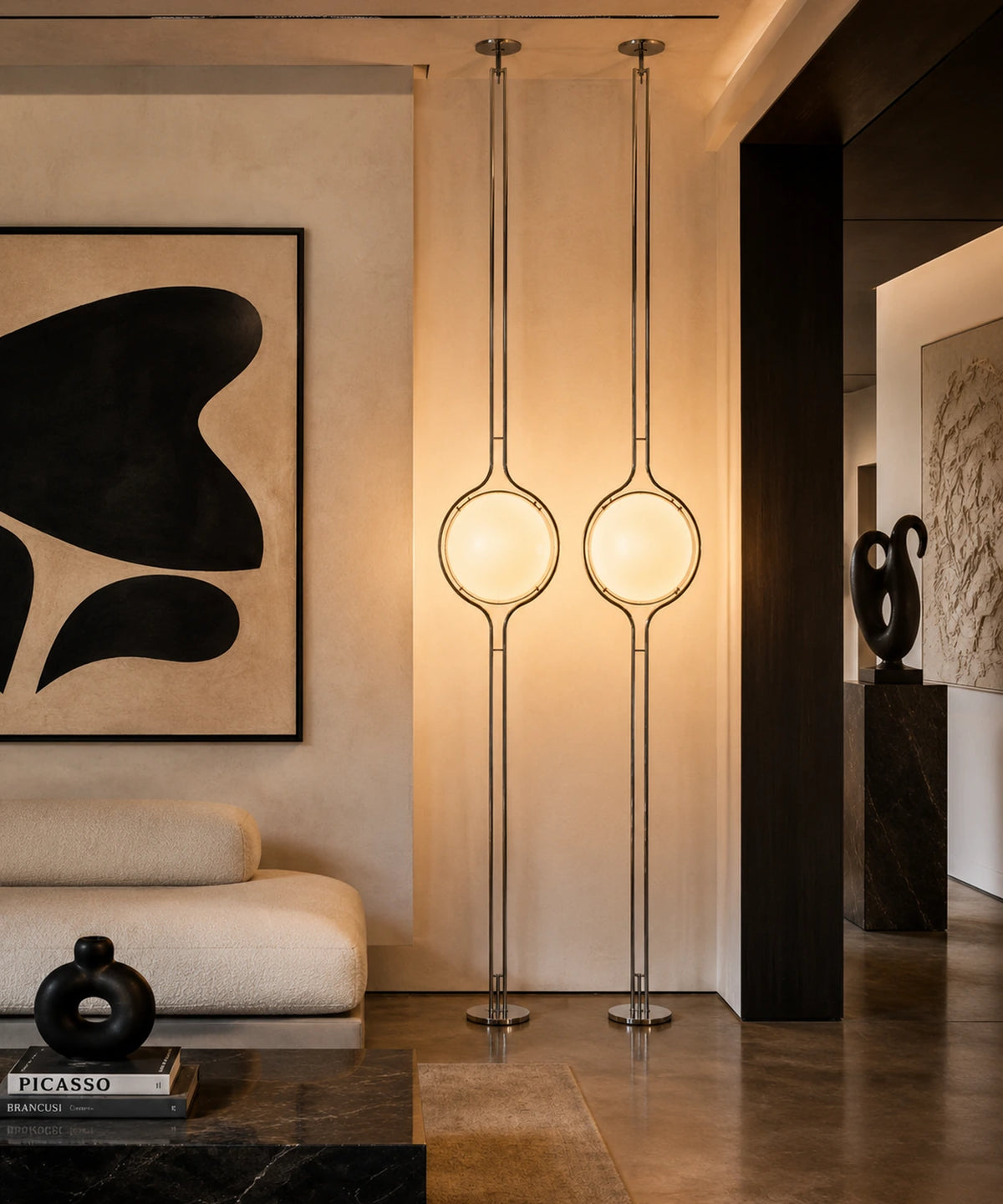 Deux lampadaires sol-plafond à boule opaline allumés dans un salon aux murs enduits