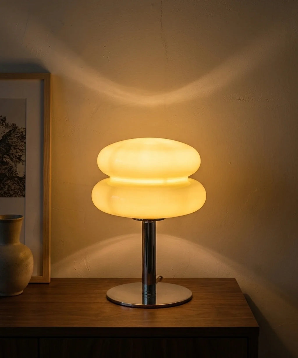 Lampe à poser verre soufflé allumée le soir, halo chaud projeté sur le mur en enduit