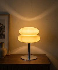 Lampe à poser verre soufflé allumée le soir, halo chaud projeté sur le mur en enduit