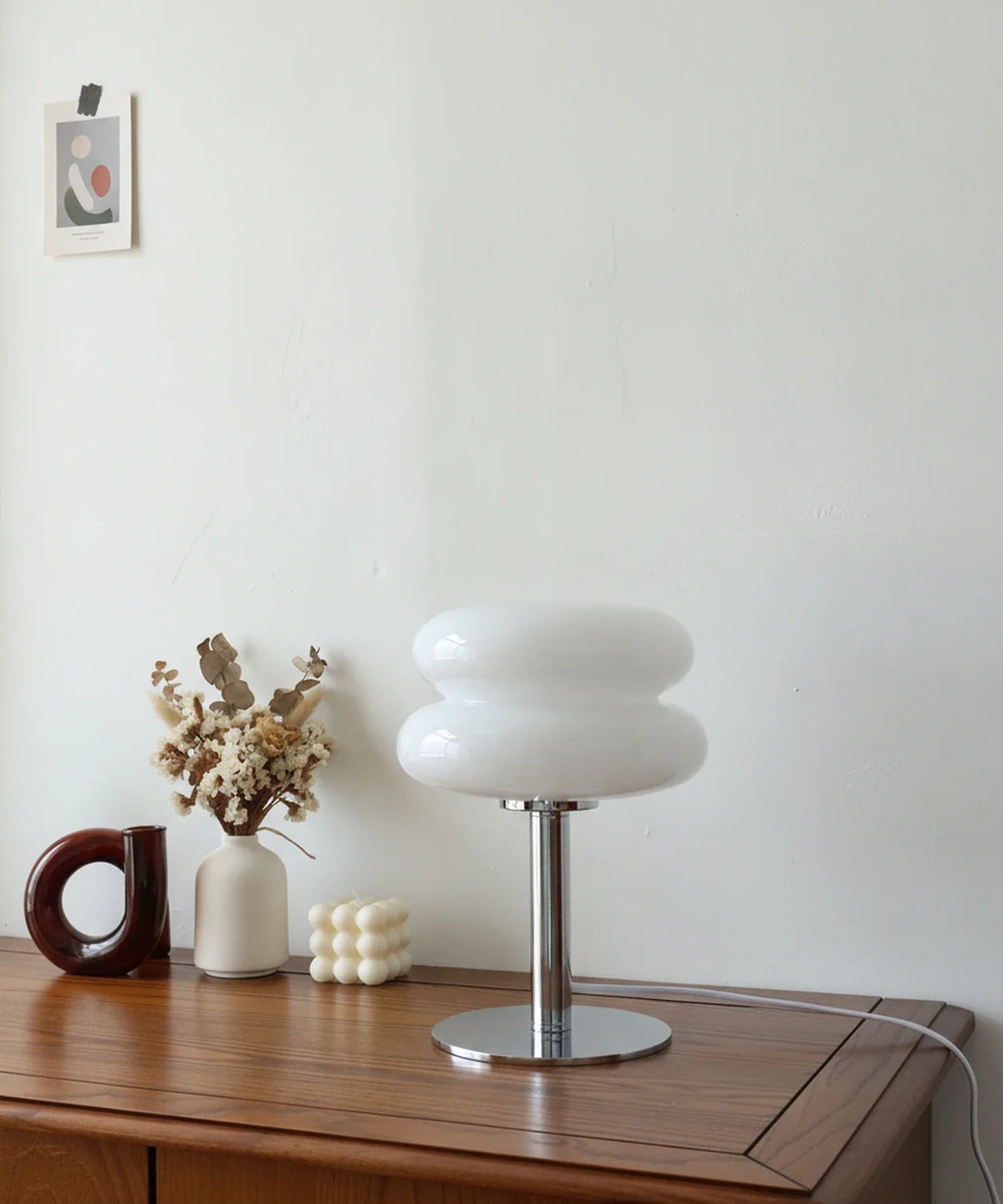 Lampe à poser verre soufflé blanc opalin sur pied disque chromé, posée sur un buffet en noyer