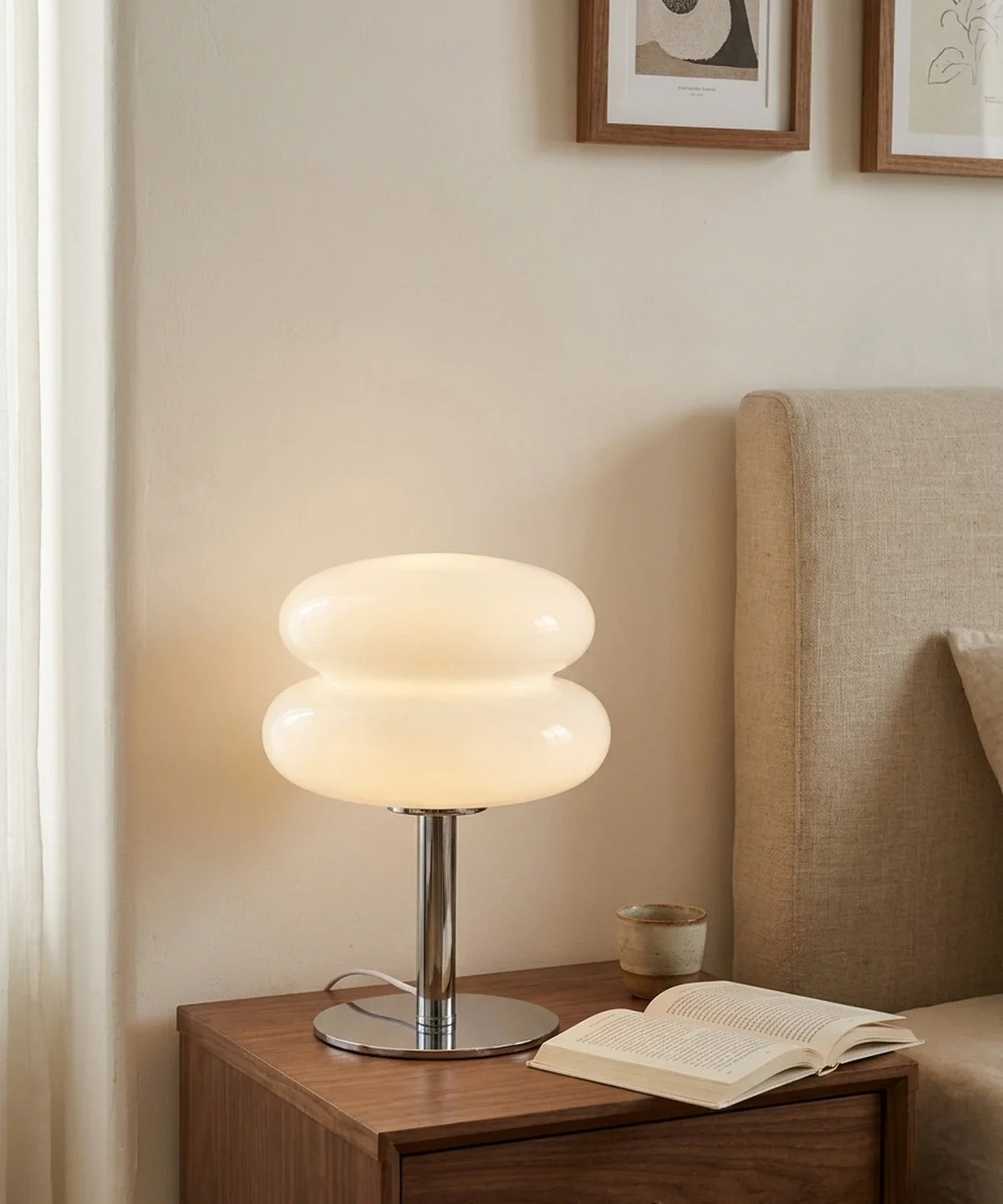 Lampe à poser verre soufflé blanc allumée sur une table de chevet en noyer, à côté d un livre ouvert
