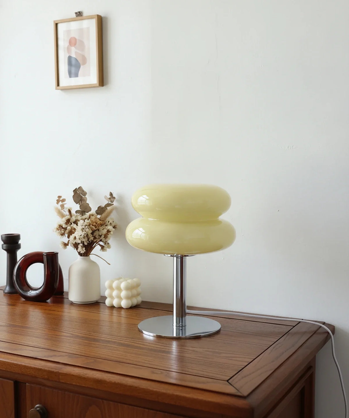 Lampe à poser verre soufflé jaune beurre sur pied disque chromé, posée sur un buffet en noyer