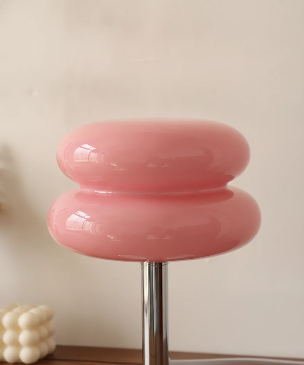 Gros plan sur les deux anneaux de verre soufflé rose et la tige chromée de la lampe à poser