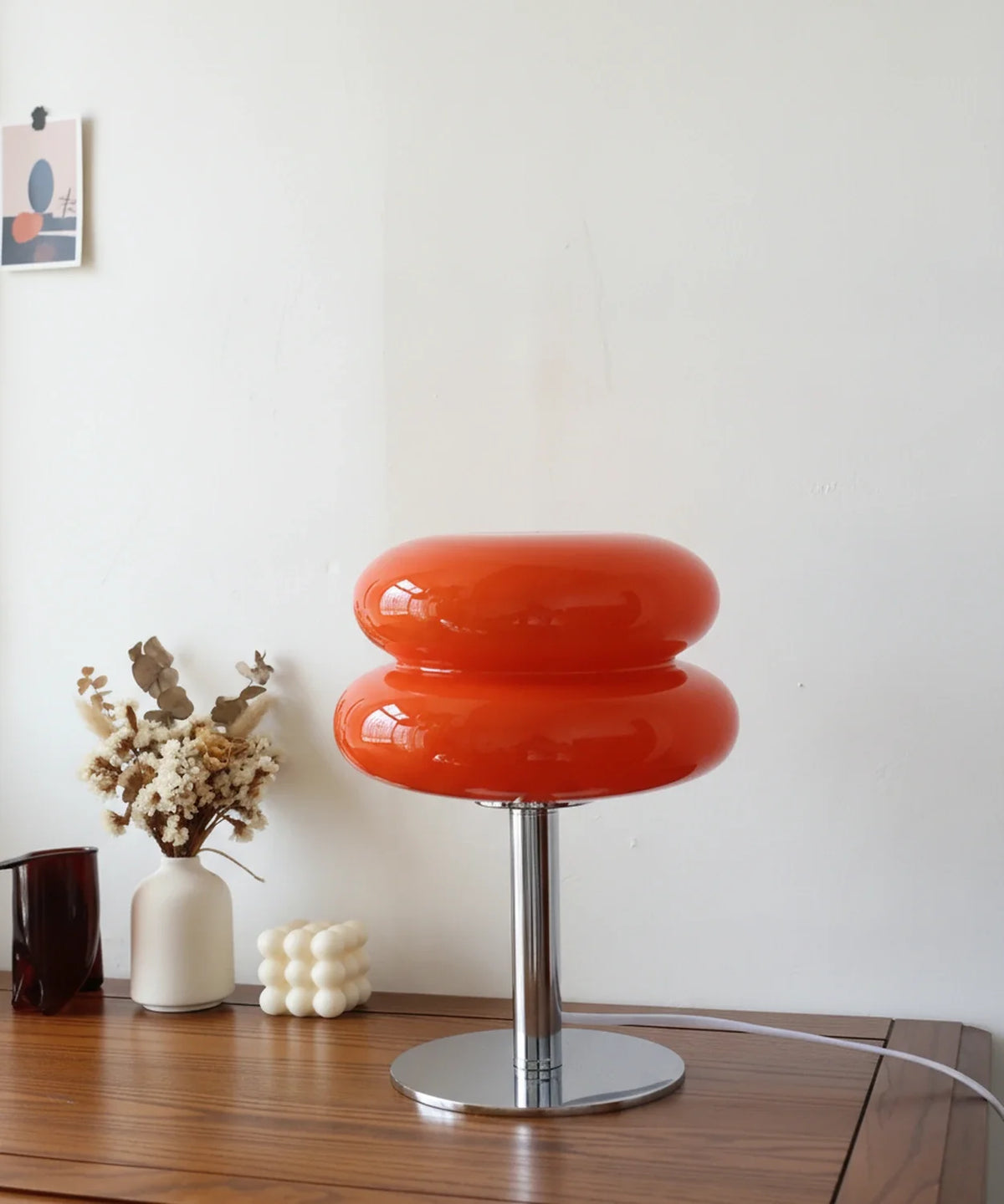 Lampe à poser verre soufflé orange ambré sur pied disque chromé, posée sur un buffet en noyer