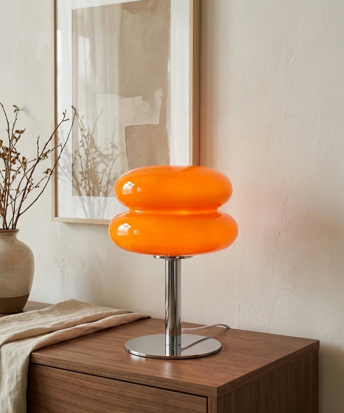 Lampe à poser verre soufflé orange allumée sur une console de salon en noyer, sous une toile abstraite