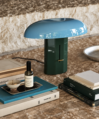 Lampe champignon bleue et verte sur une console, entourée de livres et d’objets décoratifs