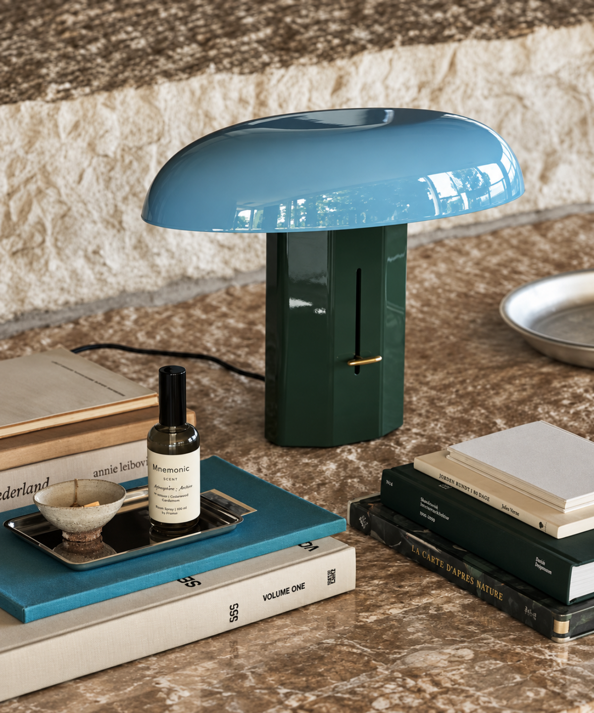 Lampe champignon bleue et verte sur une console, entourée de livres et d’objets décoratifs