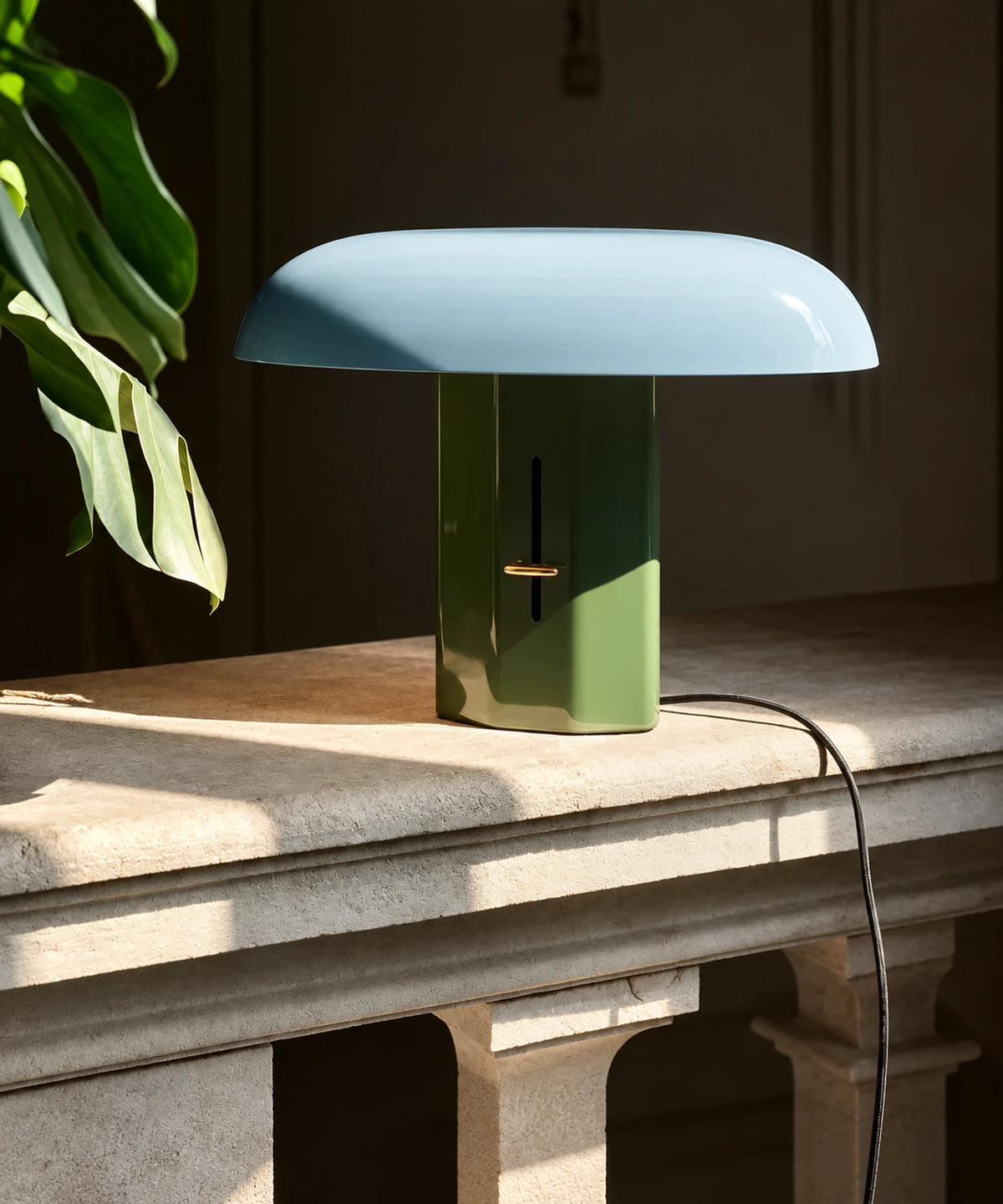 Lampe champignon bleu et vert sur un plan de travail en pierre, avec son câble visible
