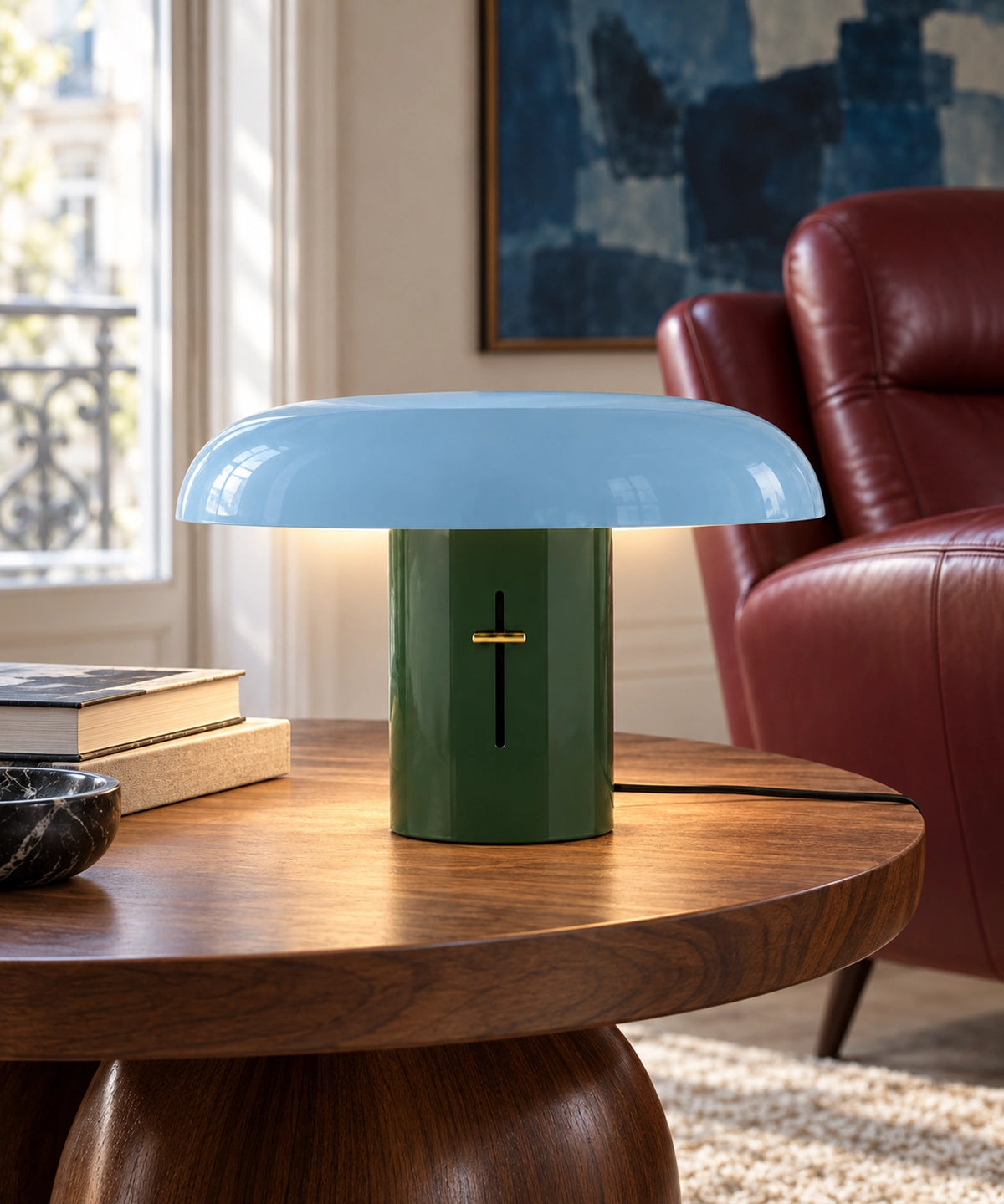 Lampe champignon bicolore en métal bleu et vert sur une table en bois près d’un fauteuil rouge