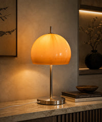 Lampe champignon orange vintage allumée le soir sur un buffet en marbre, à côté de livres