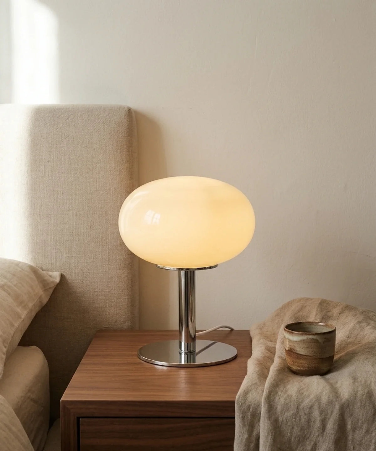 Lampe de chevet USB rose poudré allumée sur une table de nuit en noyer