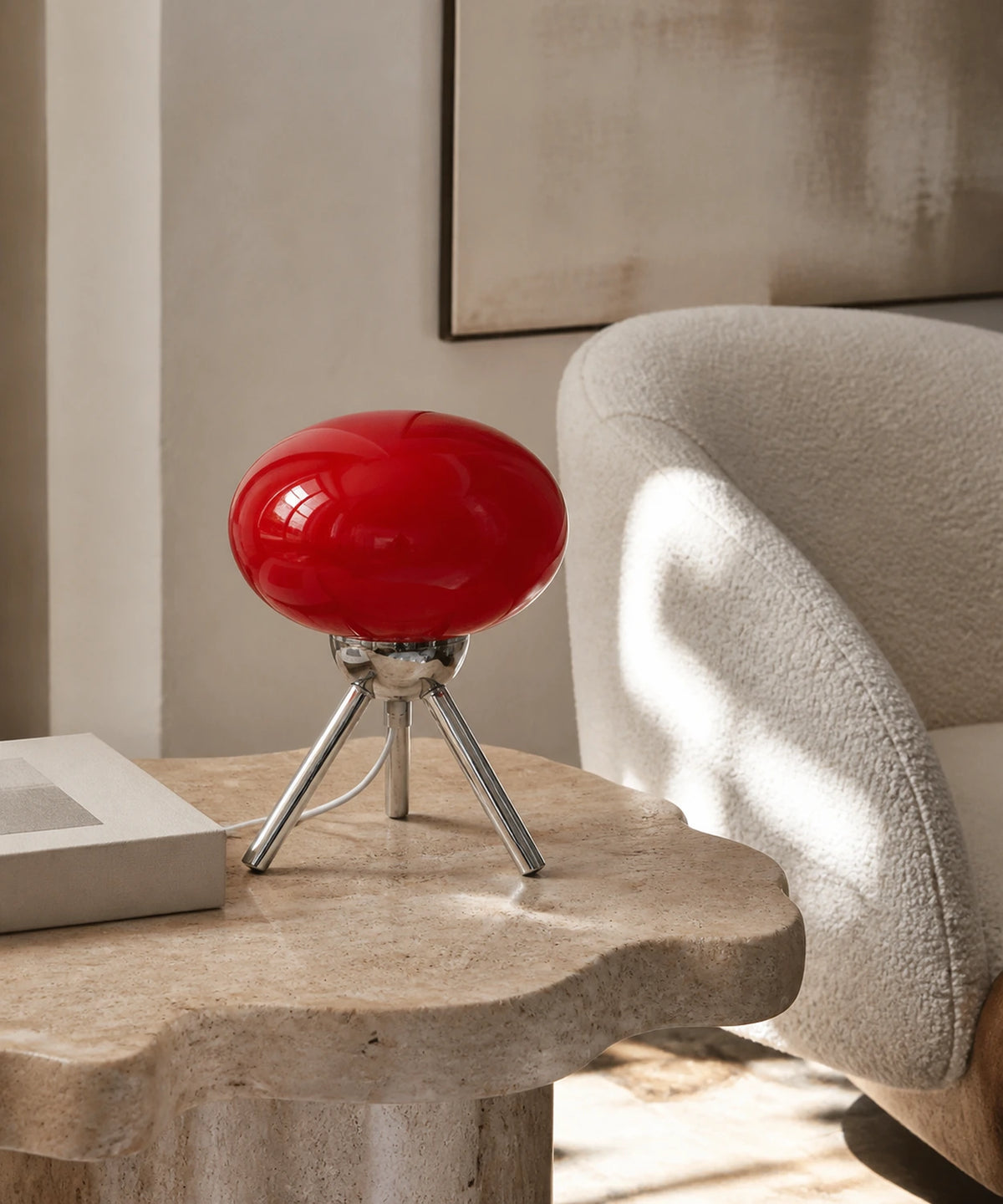 Lampe de table sans fil rechargeable USB en verre rouge sur trépied chromé, posée sur une table en travertin