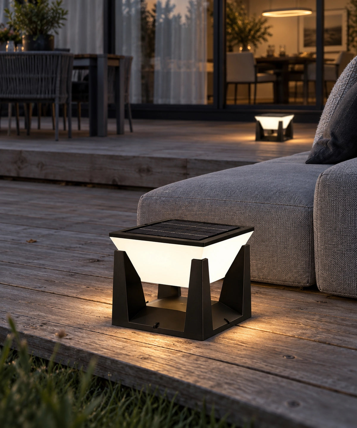 Lampe solaire carrée allumée sur une terrasse en bois, près d’un fauteuil extérieur
