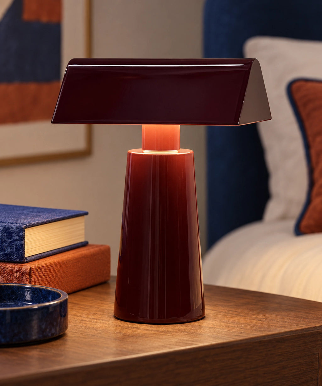 Petite lampe de table rechargeable en métal bordeaux, avec abat-jour en toit, sur une table de chevet