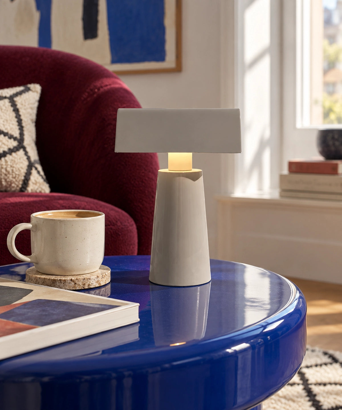 Petite lampe de table rechargeable gris clair sur une table bleue, près d’un fauteuil