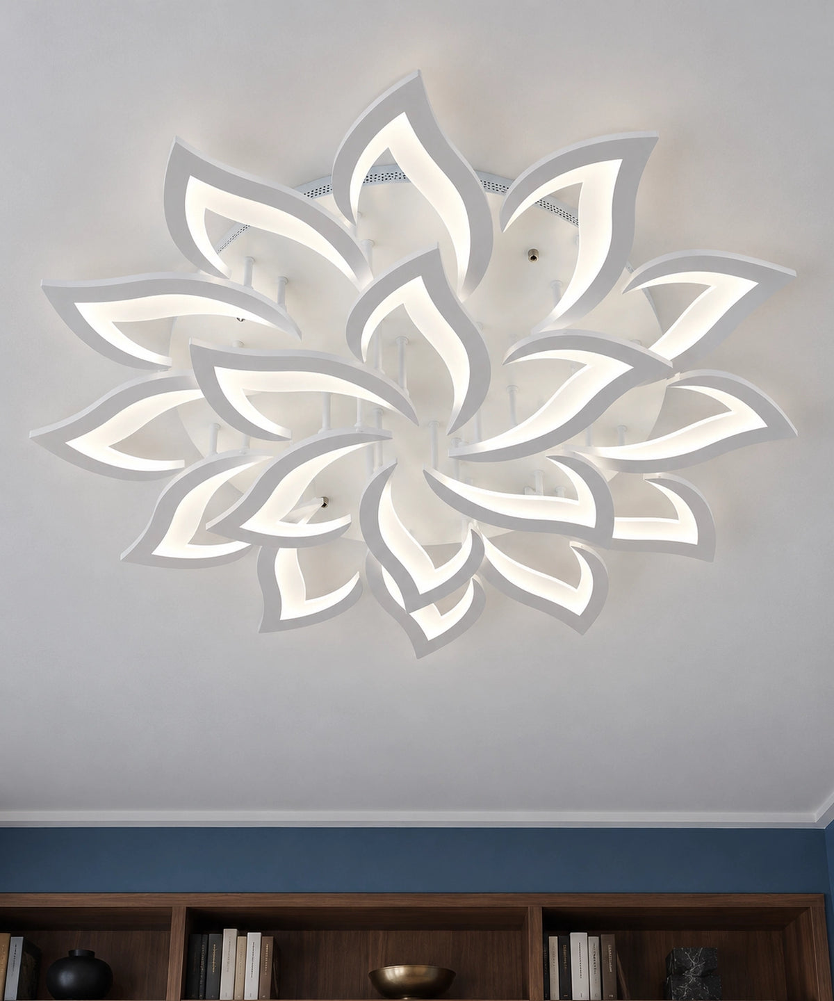Plafonnier fleur de lotus blanc à pétales ajourés, vu de dessous près d’une bibliothèque