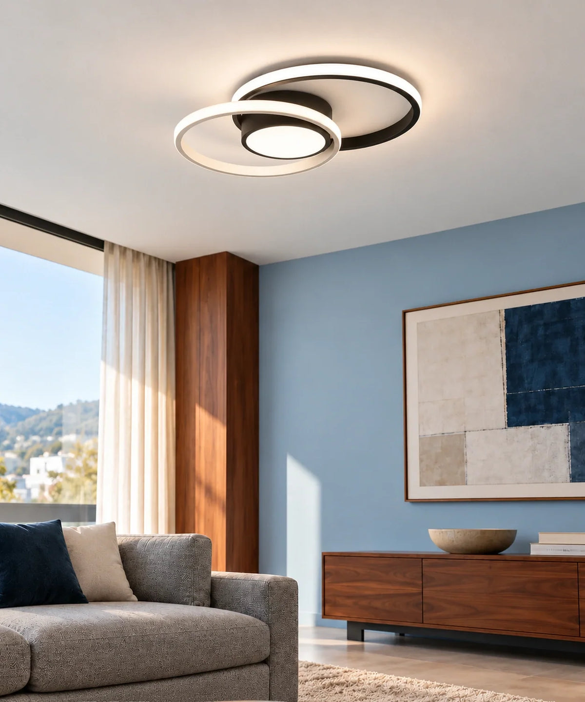 Vue rapprochée du plafonnier LED noir à deux anneaux fixé au plafond d’un salon bleu avec mobilier en bois.