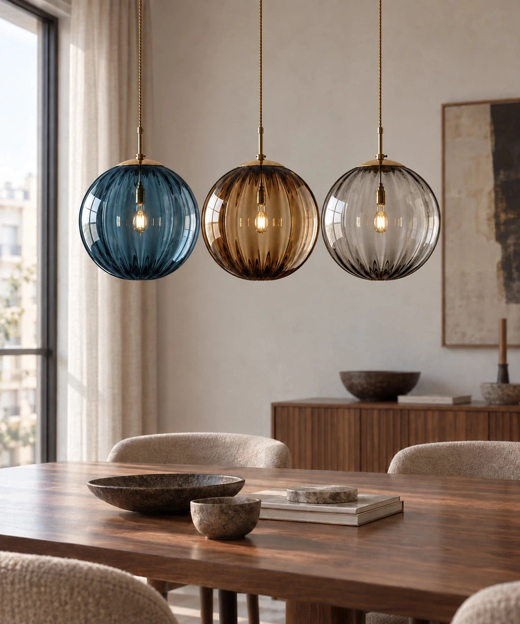 Trois suspensions boules en verre bleu, ambré et fumé au-dessus d’une table