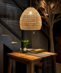 Suspension cloche en rotin beige allumée au-dessus d’une console en bois, près d’un escalier
