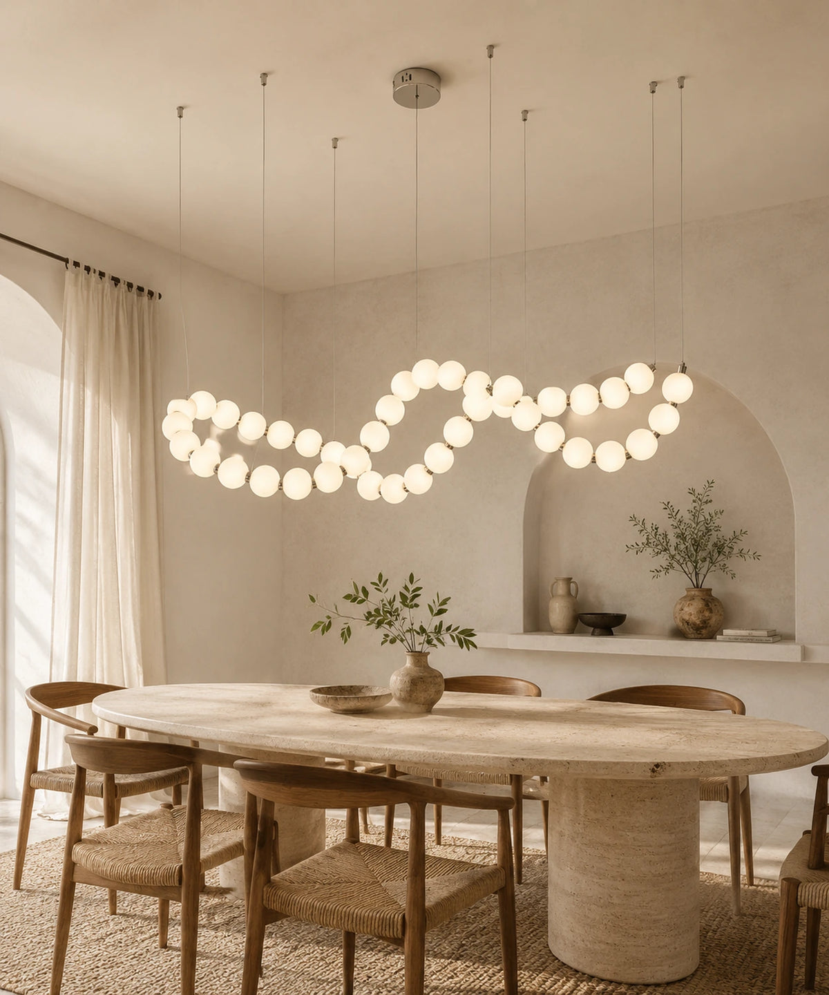 Suspension luminaire boules opalines en guirlande ondulée allumée au-dessus d’une table ovale