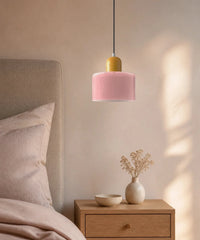 Suspension cylindre en verre rose et culot jaune moutarde au-dessus d’une table de chevet