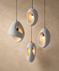 Suspension luminaire galet, ensemble de quatre galets blancs allumés devant un mur enduit